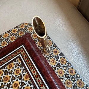 Pode incluir: Um porta-canetas decorativo com um descanso de caneta dourado. O porta-canetas est&aacute; colocado em um organizador de mesa de madeira com um padr&atilde;o geom&eacute;trico em tons de marrom, dourado e branco. O organizador tem uma moldura marrom escuro.