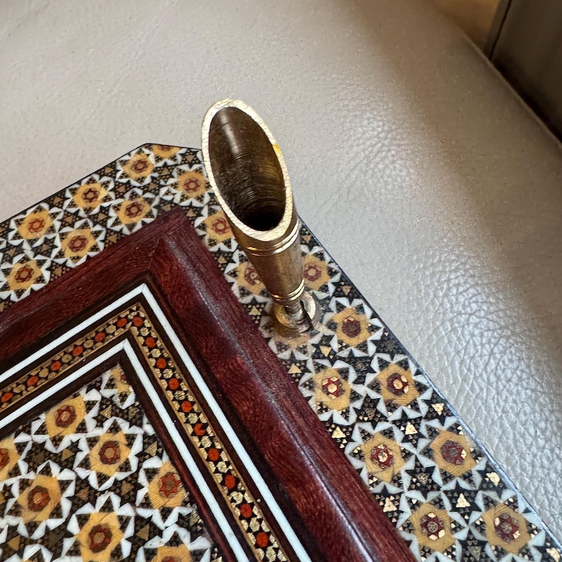 Pode incluir: Um porta-canetas decorativo com um descanso de caneta dourado. O porta-canetas est&aacute; colocado em um organizador de mesa de madeira com um padr&atilde;o geom&eacute;trico em tons de marrom, dourado e branco. O organizador tem uma moldura marrom escuro.
