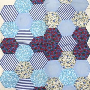 May include: A patchwork quilt made of blue, white, and red fabric. The quilt is made up of hexagonal shapes, each with a different pattern. The quilt is sewn together with white thread.