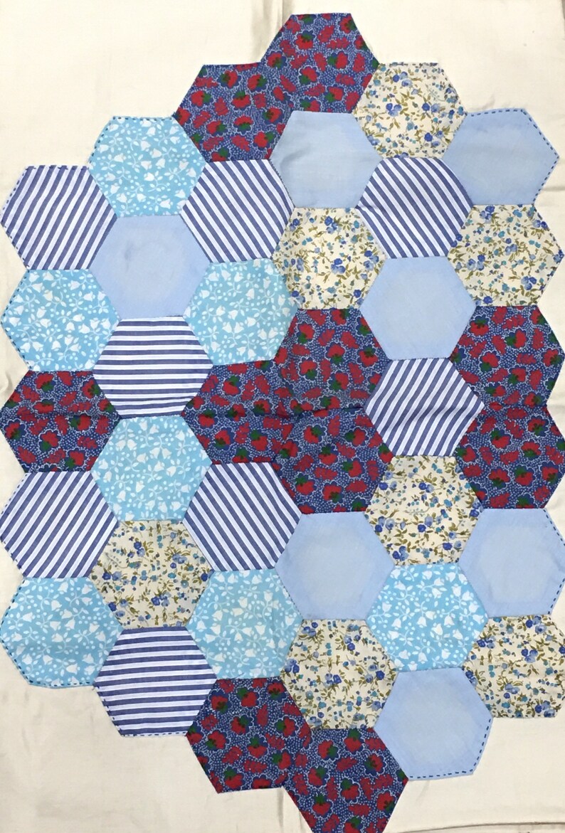 May include: A patchwork quilt made of blue, white, and red fabric. The quilt is made up of hexagonal shapes, each with a different pattern. The quilt is sewn together with white thread.