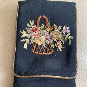 以下が含まれることがあります： 金色の縁取りと花かごの花の刺繍模様が施された黒い布製のポーチ