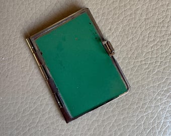 May include: A rectangular, silver-toned metal case with a bright green interior. The case has a hinged design with a clasp closure. The case is closed and appears to be empty. The case is likely a vintage item.