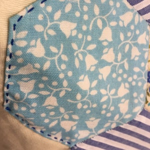 May include: A close-up of a blue and white fabric with a floral pattern. The fabric is sewn into a hexagon shape and is surrounded by other fabrics in different patterns.