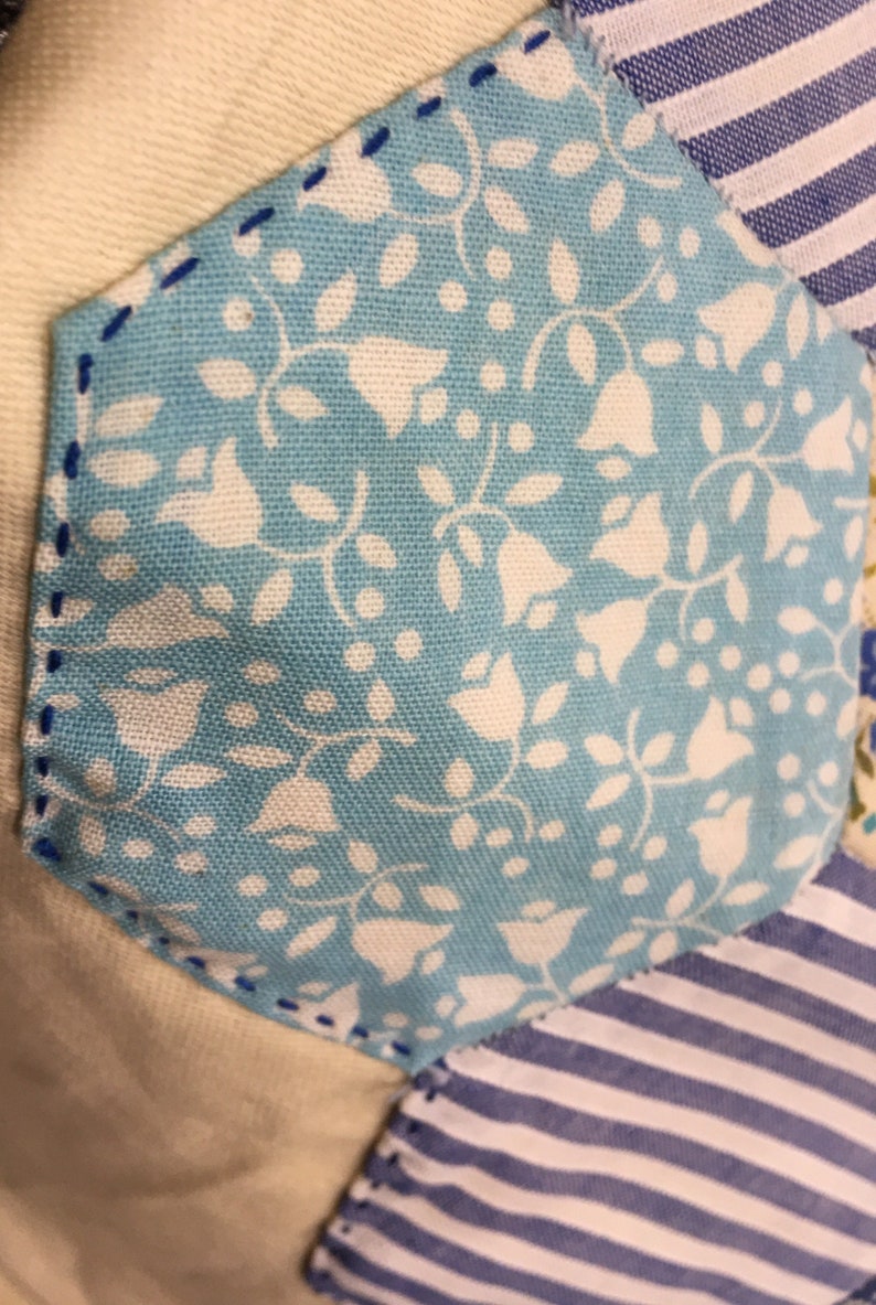 May include: A close-up of a blue and white fabric with a floral pattern. The fabric is sewn into a hexagon shape and is surrounded by other fabrics in different patterns.