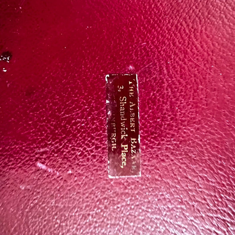 Pode incluir: Um livro encadernado em couro vermelho com um r&oacute;tulo dourado que diz "The Albert Bazaar, 3, Shandwick Place, Edinburgh."