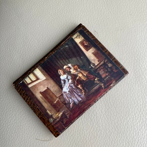 Puede incluir: Una cubierta de libro vintage con un diseño de veta de madera. La cubierta presenta una pintura de una pareja en una habitación con poca luz. El hombre lleva un traje oscuro y la mujer lleva un vestido blanco.