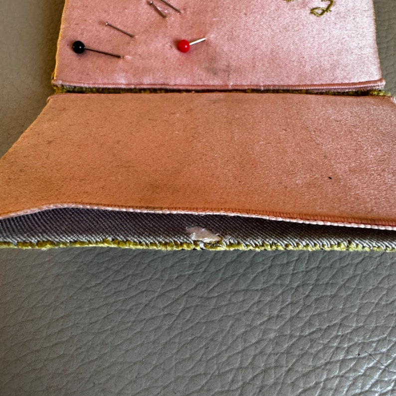 May include: A pink fabric sewing kit with a green fabric flap. The kit has a small red button and several silver pins.