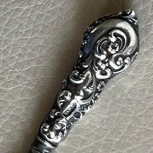 Pode incluir: Uma pega decorativa de prata, adornada com um design floral detalhado. A pega &eacute; feita de metal e tem um acabamento liso e polido.