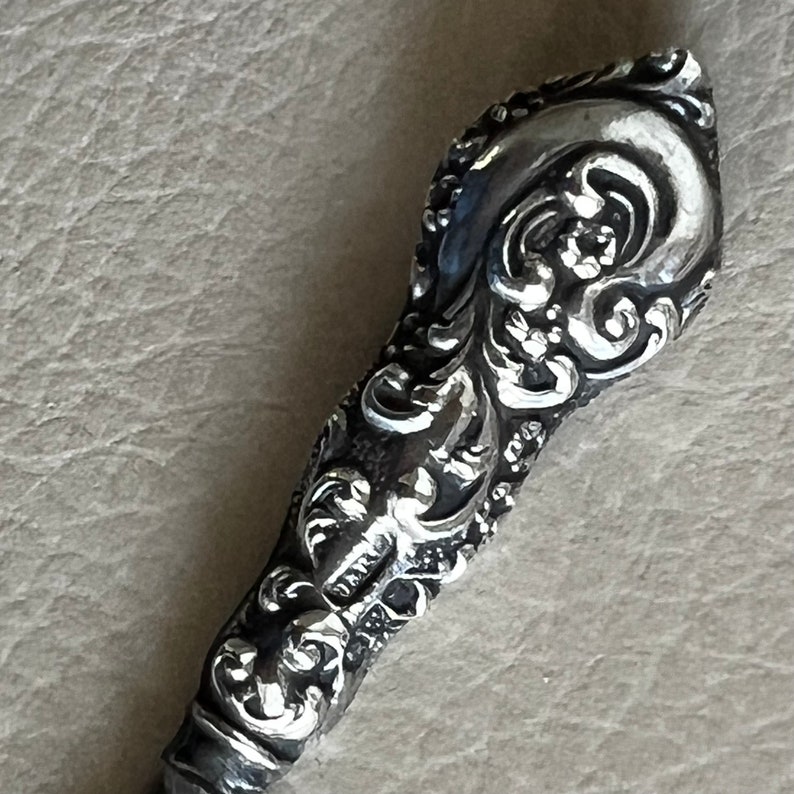 Pode incluir: Uma pega decorativa de prata, adornada com um design floral detalhado. A pega &eacute; feita de metal e tem um acabamento liso e polido.