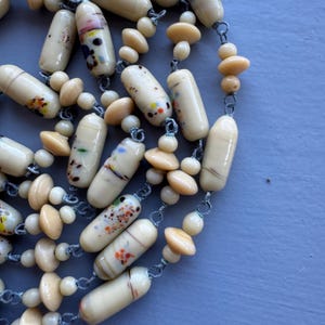 May include: A long necklace made of cream-coloured glass beads with colourful flecks. The beads are strung on a silver chain.