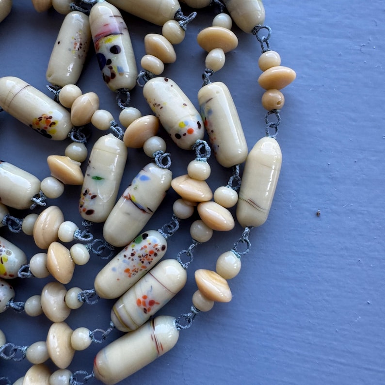 May include: A long necklace made of cream-coloured glass beads with colourful flecks. The beads are strung on a silver chain.