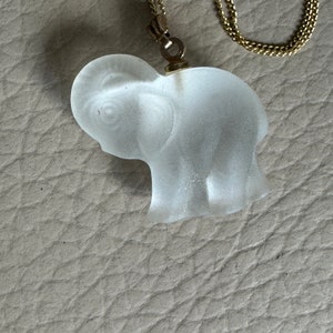 May include: A clear glass elephant pendant on a gold chain. The elephant is detailed with a textured surface and is a delicate piece of jewelry.