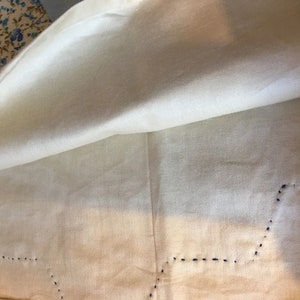 May include: A white tablecloth with a blue stitched border. The tablecloth is folded in half, revealing the underside.