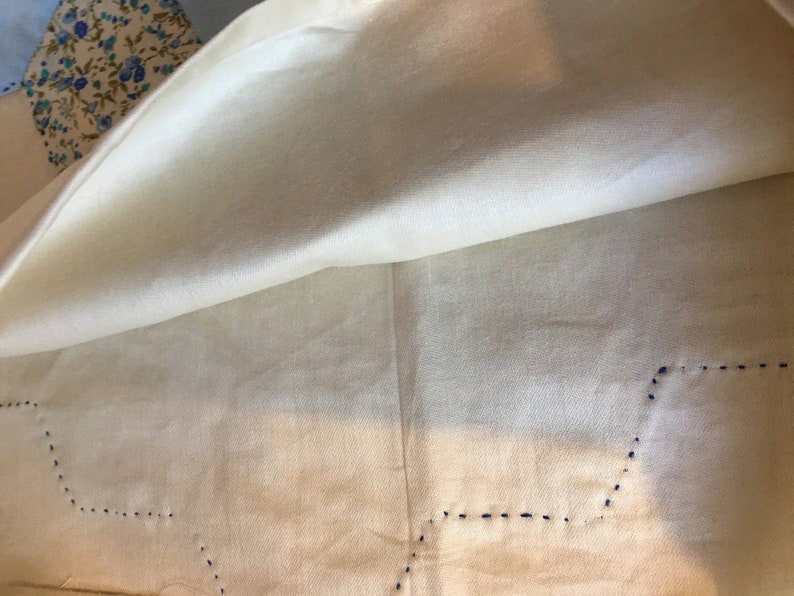 May include: A white tablecloth with a blue stitched border. The tablecloth is folded in half, revealing the underside.