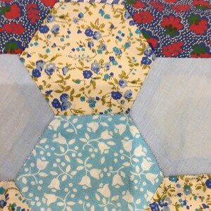 May include: A patchwork quilt made of different fabrics with floral patterns in shades of blue, red, and white. The quilt is made up of hexagonal pieces sewn together.