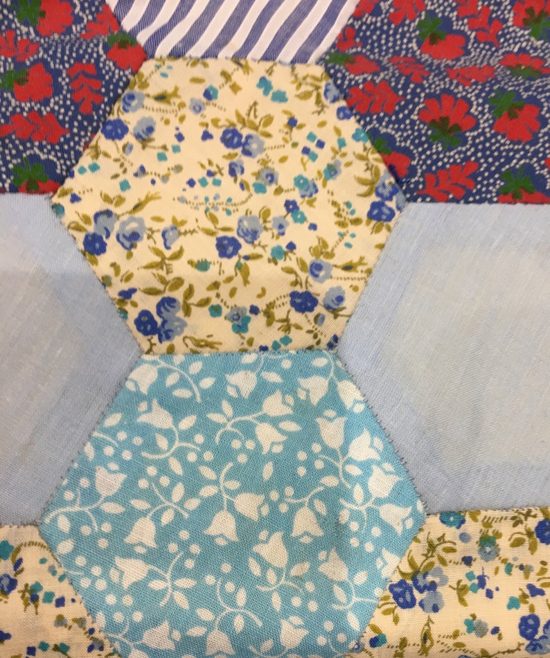 May include: A patchwork quilt made of different fabrics with floral patterns in shades of blue, red, and white. The quilt is made up of hexagonal pieces sewn together.