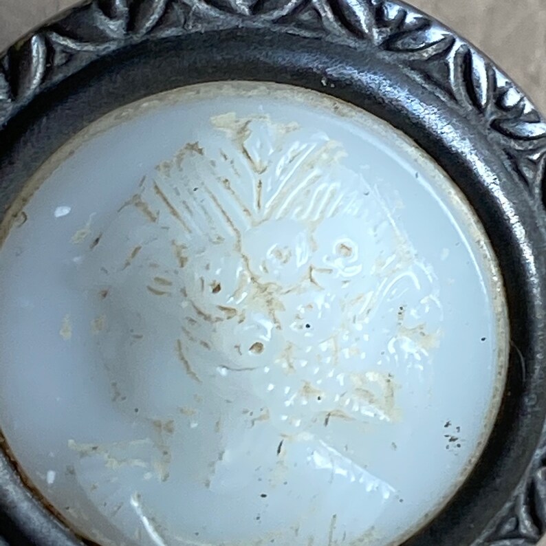 Peut inclure: Un bouton en verre blanc avec un motif floral en relief. Le bouton est mont&eacute; dans un cadre en m&eacute;tal argent&eacute; avec un bord d&eacute;coratif.