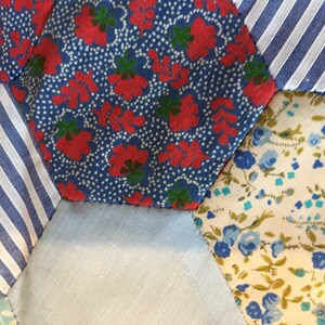 May include: Close-up of a patchwork quilt made of different fabrics. The quilt is made of hexagonal pieces of fabric in various patterns, including red and blue floral, blue and white striped, and blue and white floral.