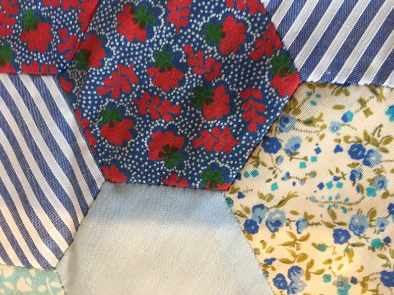 May include: Close-up of a patchwork quilt made of different fabrics. The quilt is made of hexagonal pieces of fabric in various patterns, including red and blue floral, blue and white striped, and blue and white floral.