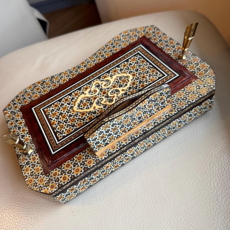Pode incluir: Um conjunto de secret&aacute;ria de madeira ornamentado com um porta-canetas e uma pequena caixa. O conjunto apresenta um padr&atilde;o de mosaico detalhado em tons de castanho, dourado e preto. O porta-canetas tem uma caneta dourada. Projetado para organiza&ccedil;&atilde;o de secret&aacute;ria.