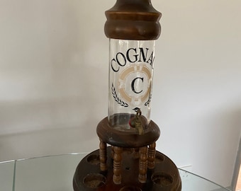 Puede incluir: Un dispensador de licor de madera con un cilindro de vidrio y una base de madera. El cilindro tiene una etiqueta que dice "COGNAC C".