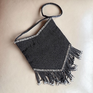 Può includere: Una borsetta nera con perline, con un piccolo manico e una lunga tracolla. La borsa ha una frangia sul fondo ed è decorata con perline color argento sulla parte superiore e sui lati.