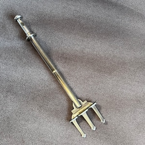 May include: A silver-toned, handheld, three-pronged tool with a long, slender handle. The tool is designed for picking up small objects.
