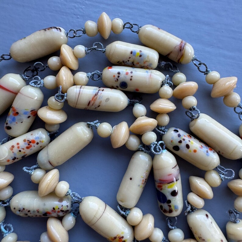 May include: A long necklace made of cream-coloured glass beads with colourful flecks and swirls. The beads are strung on a silver chain with cream-coloured spacer beads.