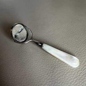 Può includere: Una lente d'ingrandimento portatile in argento con manico in madreperla.