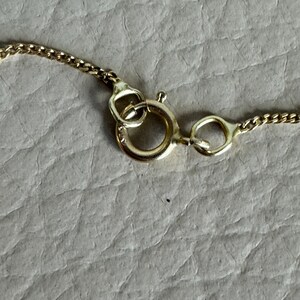 May include: Close-up of a gold chain necklace clasp. The clasp is a lobster claw style with a round ring.
