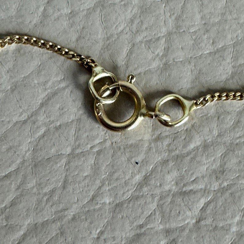 May include: Close-up of a gold chain necklace clasp. The clasp is a lobster claw style with a round ring.