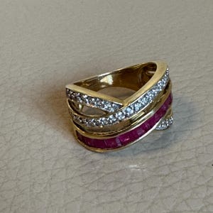 May include: A gold ring with a criss-cross design featuring a row of pink stones and a row of clear stones.