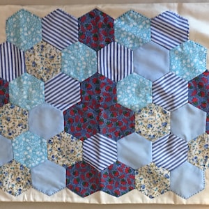 May include: A pillow with a hexagonal pattern made of fabric scraps in blue, white, and red. The fabric scraps have different patterns, including stripes, polka dots, and floral prints.