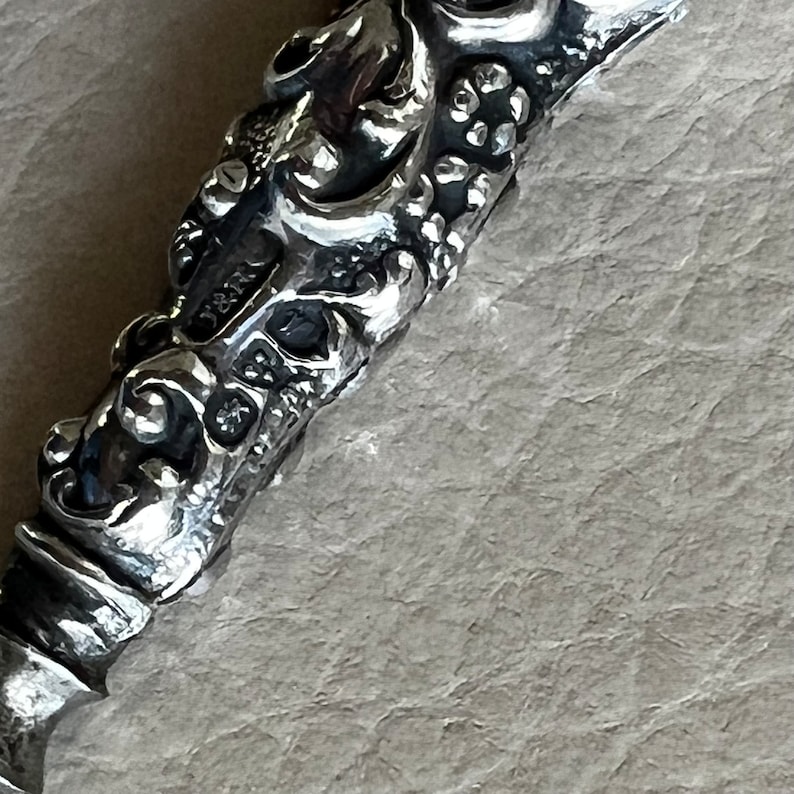 Pode incluir: Close-up de uma pega decorativa de prata adornada com detalhes intrincados.