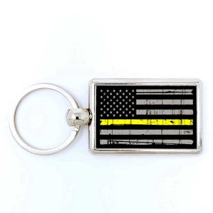 May include: A silver key chain with a rectangular metal tag featuring a distressed American flag with a thin yellow stripe across the middle.