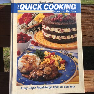 May include: A cookbook titled "Taste of Home's Quick Cooking Annual Recipes" with a photo of a chocolate cake with raspberries on top and a plate of mashed potatoes, gravy, a hamburger patty, and corn.