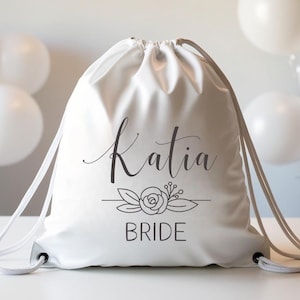 May include: White drawstring bag with the name "Katia Bride" printed in black cursive font with a floral design.