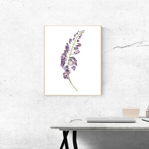 以下が含まれることがあります： 白い背景に紫色の藤の花の房を描いた詳細な水彩画の壁掛けアートプリント。薄い明るい木製のフレームに収められており、繊細な花びらと緑の茎が特徴です。アートワークは壁に飾られた状態で表示されています。