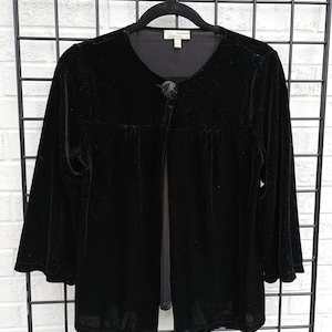 May include: A black velvet jacket with a round neckline and three-quarter sleeves. The jacket has a single button closure and is hanging on a black hanger. The brand name "Chouix" is visible on the label.