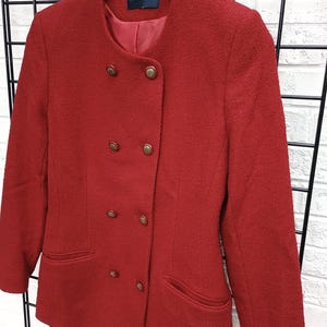 May include: A red double-breasted blazer with gold-colored buttons and two front pockets. The blazer has a textured fabric and a round neckline. The brand name "ALEXON" is visible on a tag inside the collar.