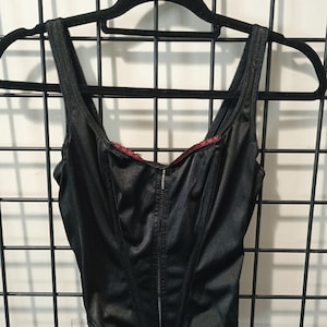May include: A black satin corset with a zipper down the front and red lace trim around the neckline.