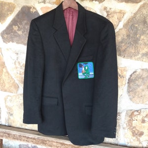 May include: A black blazer with a green patch featuring a cartoon image of two people sitting on a bench. The patch is on the left side of the blazer.