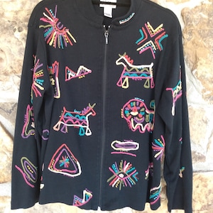 May include: Black zip-up jacket with colorful embroidered geometric designs and animal figures. The jacket has a stand-up collar and long sleeves.