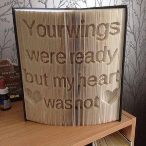 May include: A book with the pages folded to create a 3D design of the words "Your wings were ready but my heart was not". The words are surrounded by two hearts.