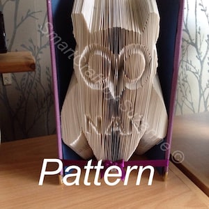 May include: A book folded into the shape of an owl, with a purple ribbon and the word "Pattern" printed below. The owl is made from the pages of a book and has a detailed design.