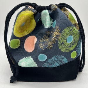 May include: A black drawstring bag with a black bottom and a colorful abstract print featuring green, blue, pink, and gold circles and shapes.