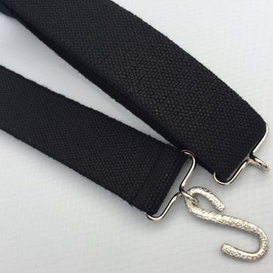 May include: Two black fabric straps with silver metal hooks. The straps are woven and have a textured surface.