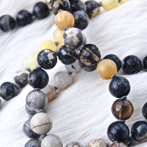 Puede incluir: Primer plano de un collar de cuentas hecho con piedras negras, marrones y blancas. El collar está sobre una superficie de pelo blanco.