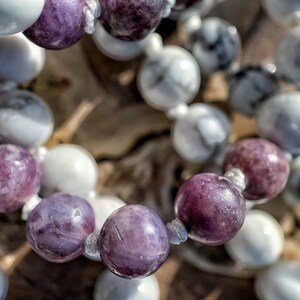 May include: A close-up of a beaded necklace with alternating white and purple beads. The beads are round and have a smooth, polished finish.