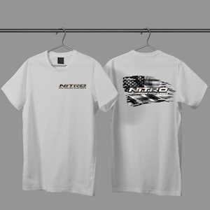 May include: Two white t-shirts hanging on a rack. The front of the first shirt has the text "NITRO PERFORMANCE BASS BOATS". The back of the second shirt has a black and white American flag design with the text "NITRO PERFORMANCE FISHING BOATS".